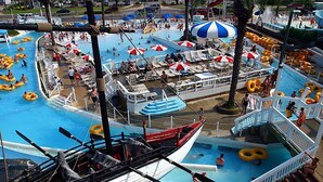 Una gran piscina exterior amb diverses línies, envoltada de gandules i ombrelles.