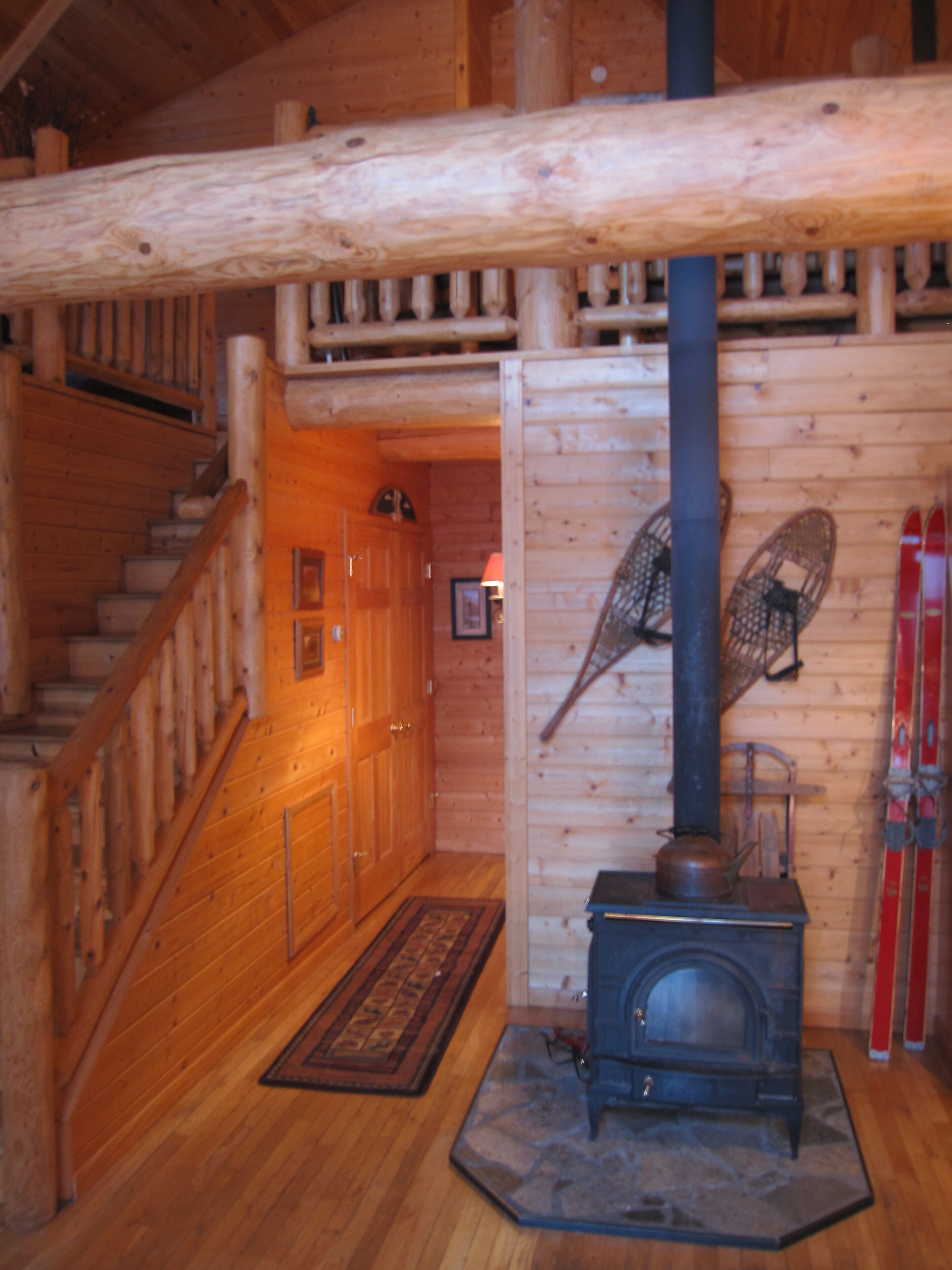 Ein Holzblockhaus-Innenraum mit Treppe, Kamin und Ski, die an der Wand lehnen.