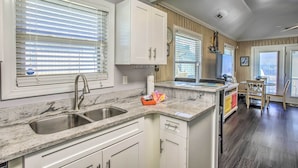 A kitchen with a double sink, white cabinets, a marble countertop, and a dining area with a table and chairs. - Walk to Apache Pier: Coastal Condo w/ Pool Access (Myrtle Beach)