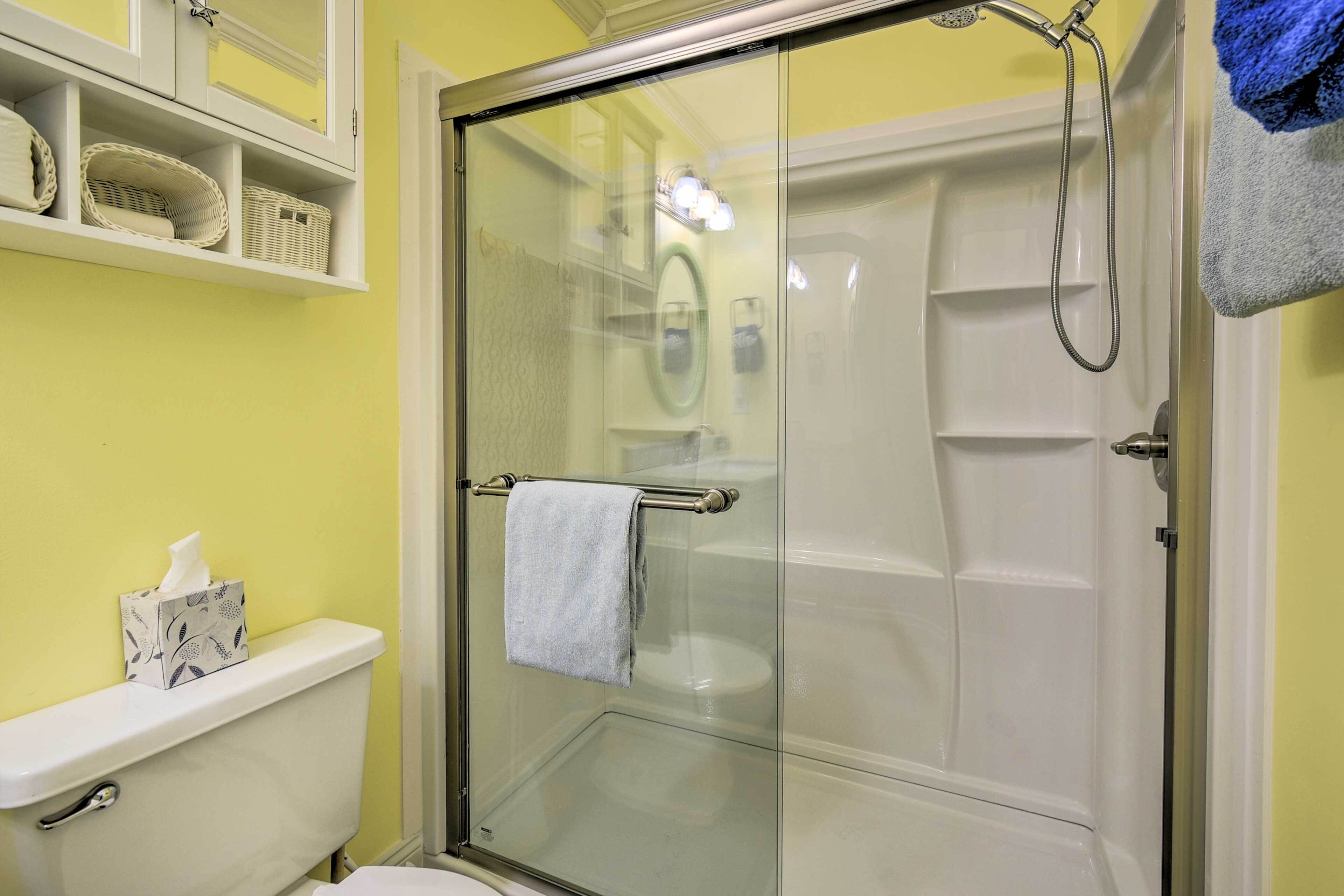 Et badeværelse med en glasvæg omkring brusenichen, toilet og en hylde med kurve.