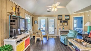 A cozy living room with a TV, wooden furniture, a ceiling fan, and a view of the outdoors. - Walk to Apache Pier: Coastal Condo w/ Pool Access (Myrtle Beach)
