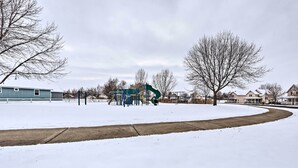 En snötäckt park med en lekplats och hus i bakgrunden.