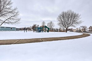 Un parco innevato con un'area giochi e case sullo sfondo.