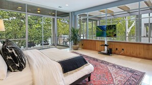 A modern bedroom with a large bed, a ceiling fan, and a view of a lake through large windows.