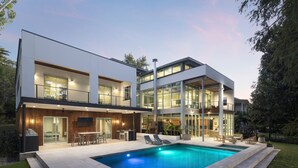 A modern two-story house with a swimming pool, outdoor seating, and a well-lit patio area.