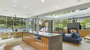 A modern kitchen with a large island, wooden cabinets, and a built-in oven. There is a seating area with a blue sofa and a fireplace.