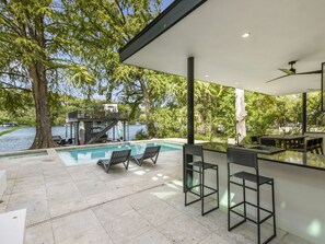 Ein moderner Poolbereich im Freien mit Liegestühlen und einer Bar, mit Blick auf einen See und umgeben von Bäumen.