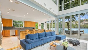 A modern open-plan living area with a blue sofa, wooden chairs, and a coffee table.