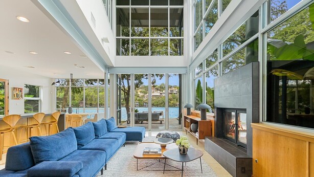 A spacious living area with a blue sofa, a fireplace, and large windows offering a view of the outdoors.
