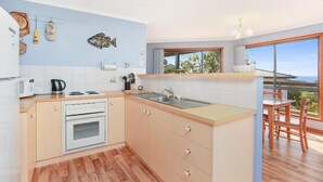 A modern kitchen with a wooden floor, a built-in oven, a sink, and a window overlooking the sea.