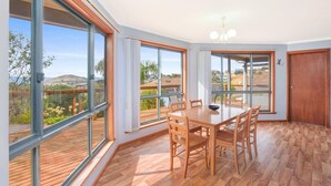 A spacious room with large windows, a wooden dining table, and a view of a coastal landscape.