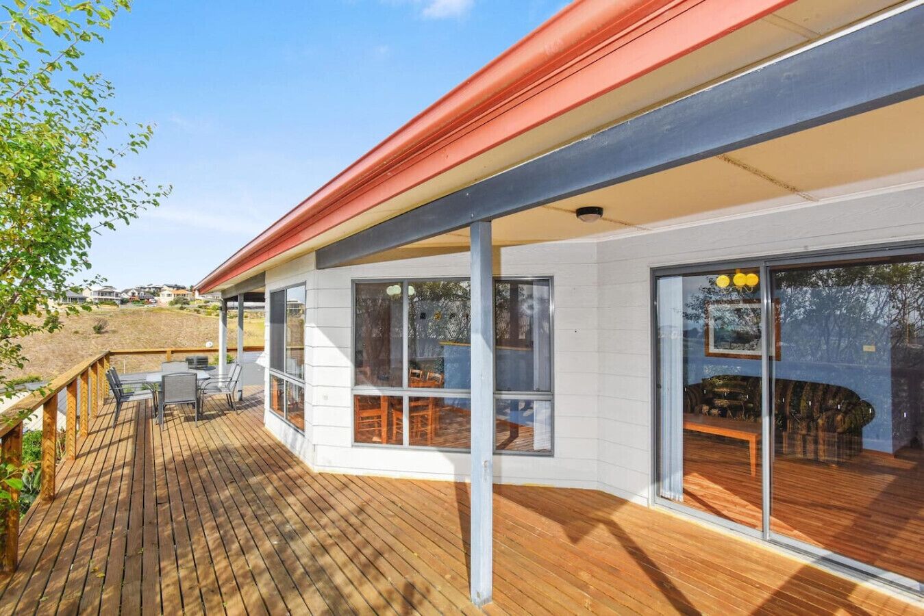 Una casa moderna con terraza de madera, grandes puertas correderas de vidrio y techo rojo.
