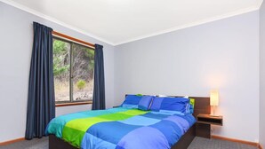 A bedroom with a bed, a window, and a nightstand with a lamp.