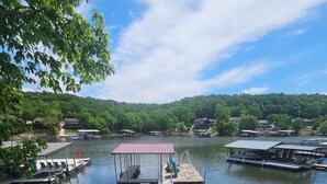 A dock with a covered seating area, a boat, and a view of a lake surrounded by houses. - COMPLETELY REMODLED!! Gorgeous 5 BR/5.5 BA in NO WAKE cove, Dock w/12'x30' slip (Sunrise Beach)