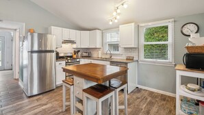 Une cuisine moderne avec des meubles blancs, des appareils en acier inoxydable, une table à manger en bois et une fenêtre donnant sur un paysage verdoyant.