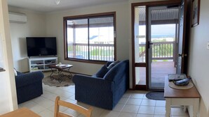 Een woonkamer met een televisie, twee banken, een eettafel en een balkon met uitzicht.