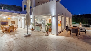 Ein modernes Haus mit einer Terrasse, die einen Esstisch, Stühle und Kübelpflanzen zeigt.