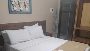 Un lit bien fait, avec du linge de lit blanc et une couverture marron, une tête de lit en bois et une petite table de chevet.