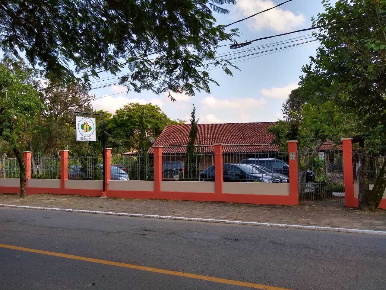 Propiedad cercada con un edificio de techo rojo, un cartel y coches aparcados.