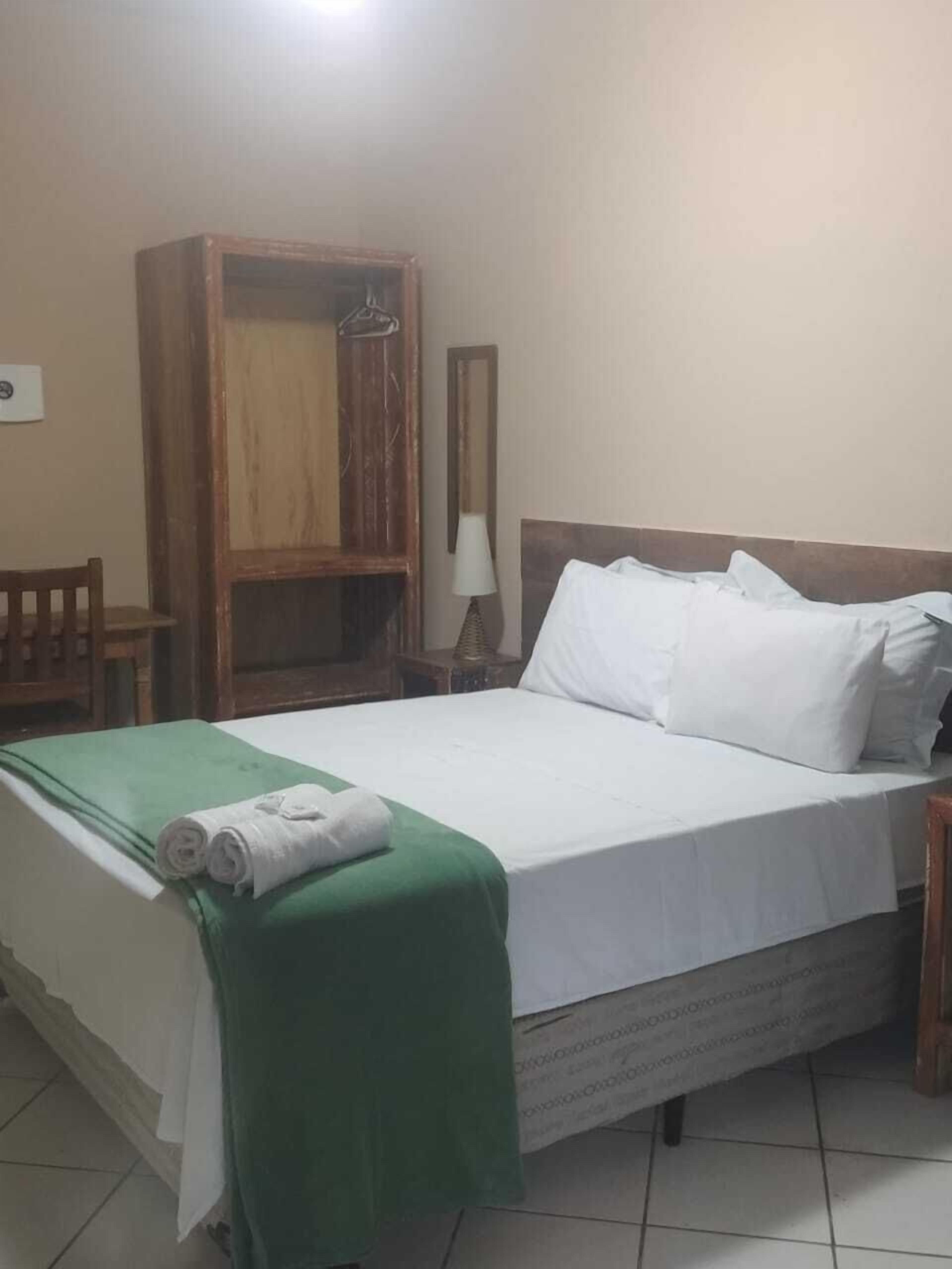 Ein Hotelzimmer mit einem Bett, einem grünen Handtuch, einem Holzschrank, einem Nachttisch und einer Lampe.