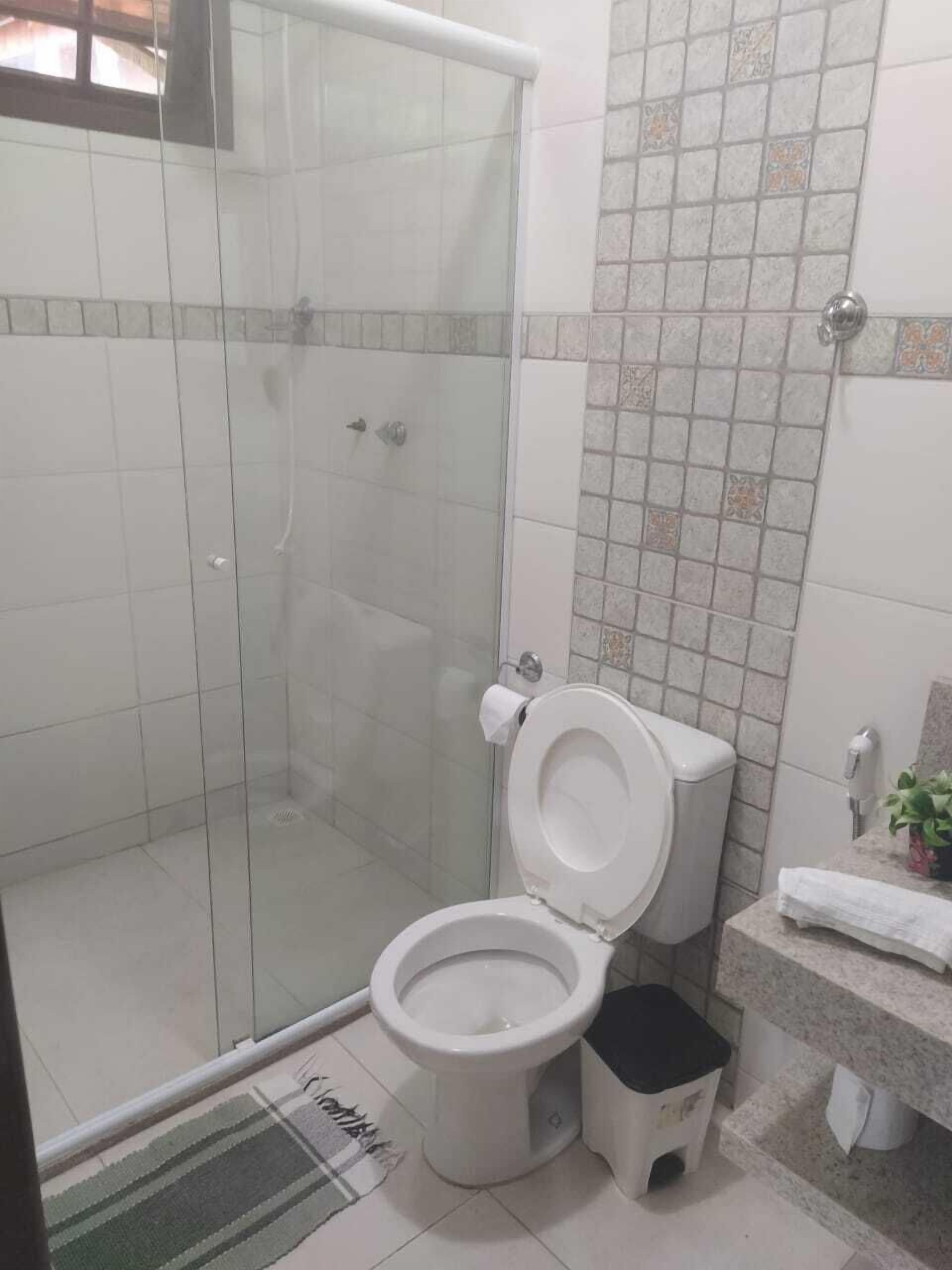 Un baño con ducha de vidrio, inodoro y lavamanos con un pequeño taburete.