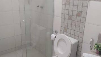 Un baño con ducha de vidrio, inodoro y lavamanos con un pequeño taburete.