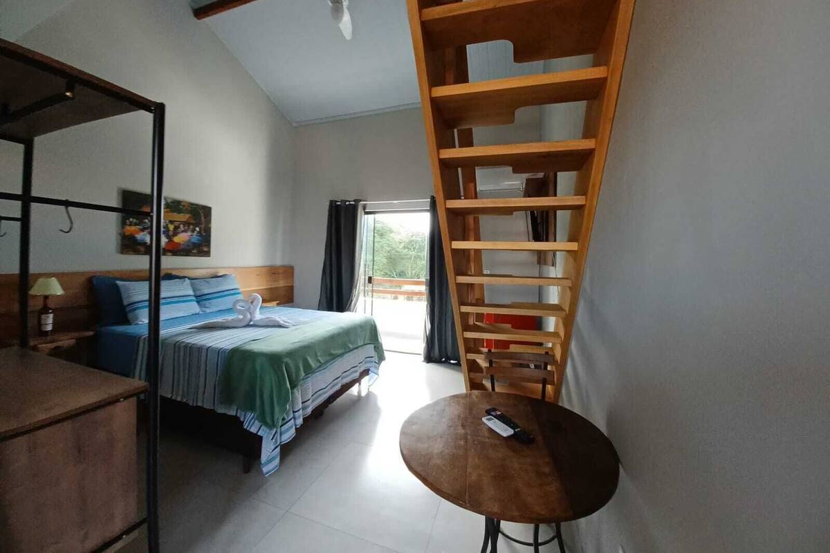 Quarto com uma cama, uma escada de madeira, uma mesa pequena e um ventilador de teto.