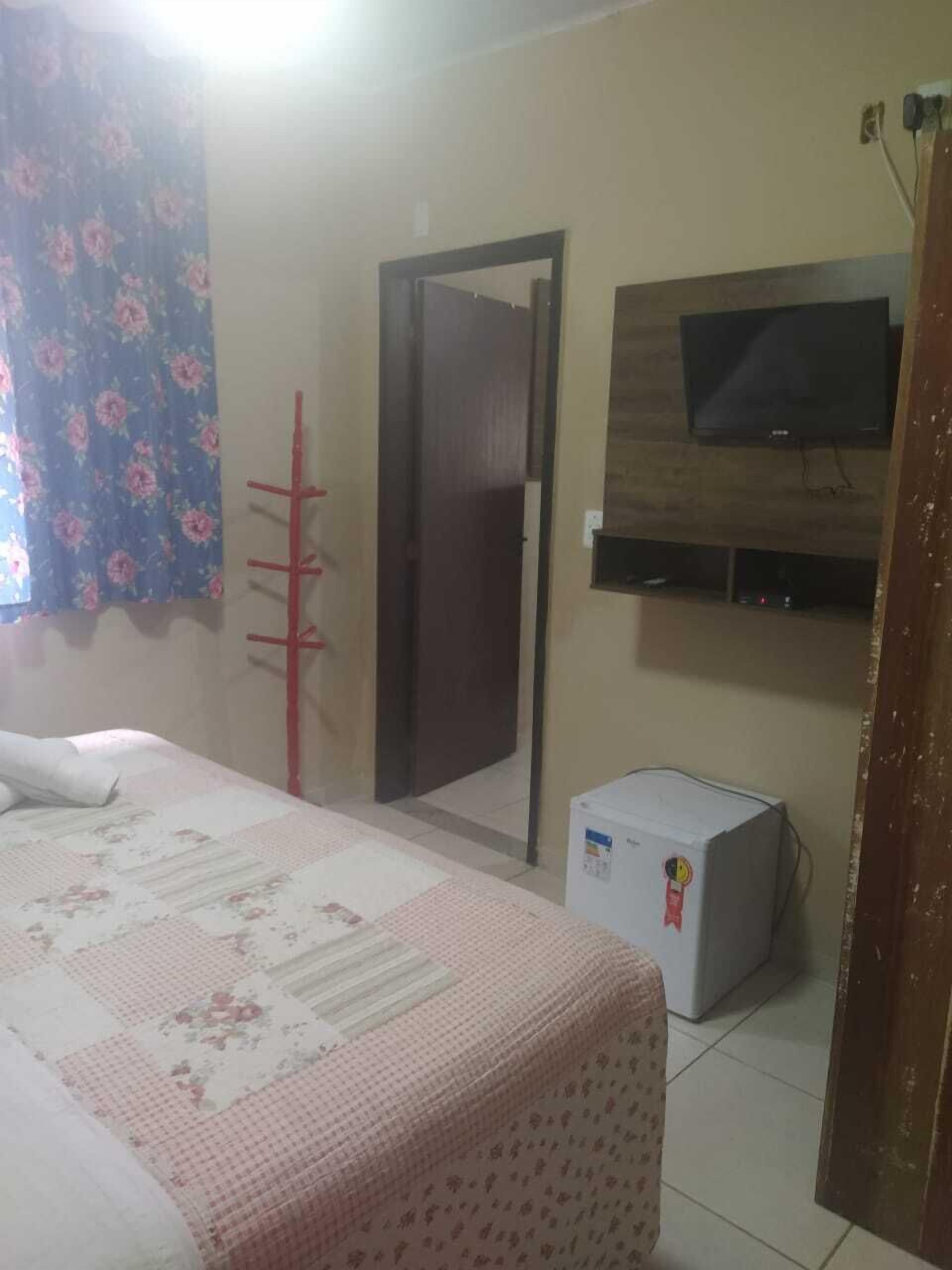 Quarto com cama, televisão na parede e um frigorífico pequeno.