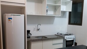 Cocina compacta con refrigerador, estufa, pileta y un pequeño comedor con taburetes.