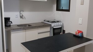 Una cocina compacta con armarios blancos, estufa a gas, cafetera y una ventana pequeña.