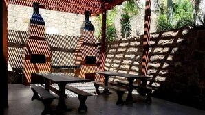 Un patio al aire libre con mesas y bancos de madera, un muro con diseño y una pared de piedra con vegetación.