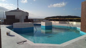 Una piscina en la azotea con agua cristalina y azul, rodeada por una solana con baldosas y un muro de ladrillo.