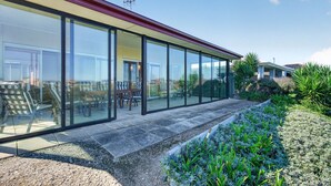 Ein modernes Gebäude mit großen Glasfenstern, einer Terrasse mit Gartenmöbeln und einem gepflegten Garten.