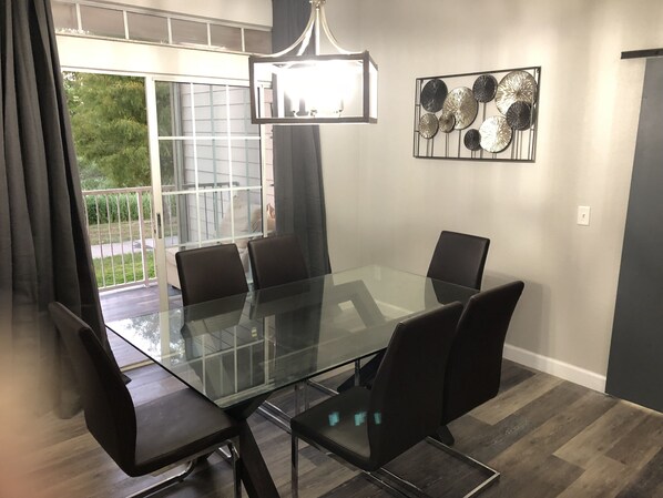Un comedor moderno con una mesa de vidrio y sillas negras, una araña y un elemento decorativo en la pared.