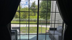Une vue à travers une fenêtre à carreaux, un balcon avec une balustrade blanche et une pelouse verdoyante.
