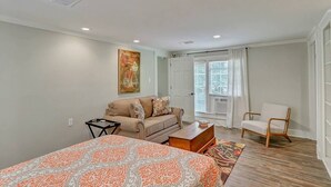 A bedroom with a bed, a sofa, a chair, a small table, and a window with curtains.