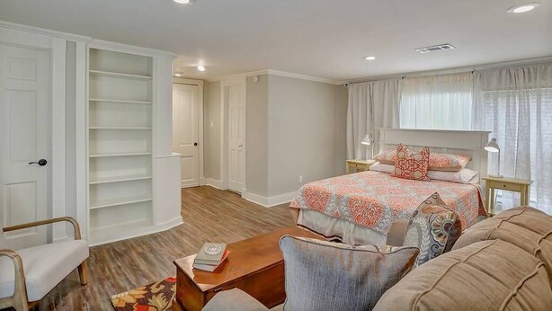 A bedroom with a bed, bedside tables, a chair, a wooden coffee table, and built-in shelving.