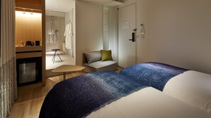 Ein Hotelzimmer mit Bett, einem kleinen Tisch, einer Sitzecke und einem Duschbereich, sowie einem Spiegel.