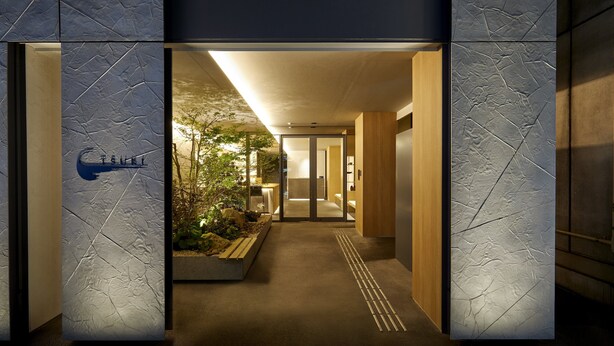 Ein moderner Hotelzugang mit einer strukturierten Wand und einem Schild mit der Aufschrift 'TSUKI'.
