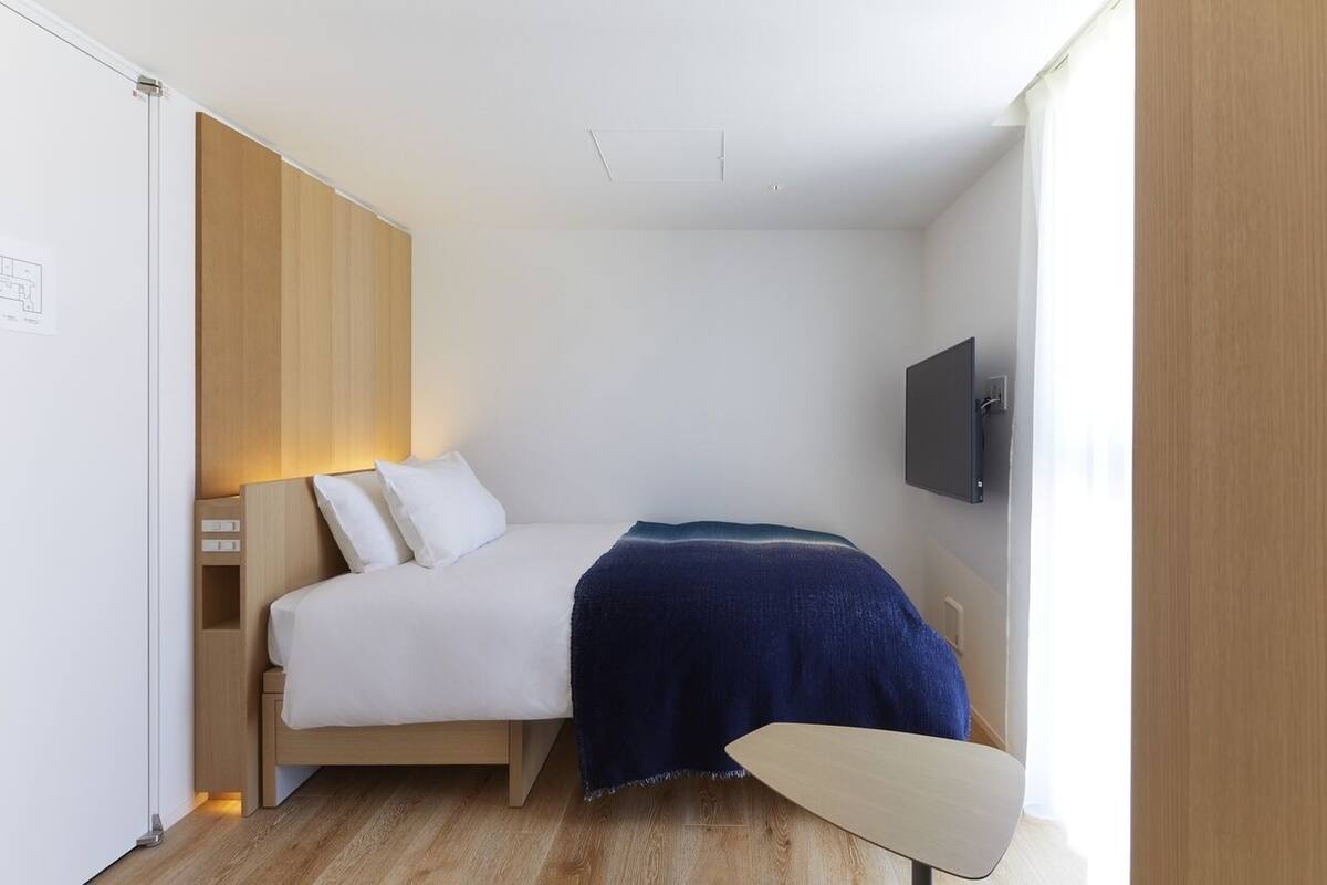 A bedroom with a bed, bedside table, lamp, TV, and a wooden wardrobe.