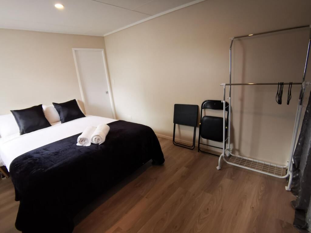Habitació d'hotel amb llit, una cadira, zona de dutxa i una porta.