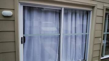 Un edificio con fachada color beige, una puerta corrediza de vidrio con cortina blanca y un pequeño respiradero encima de la puerta.