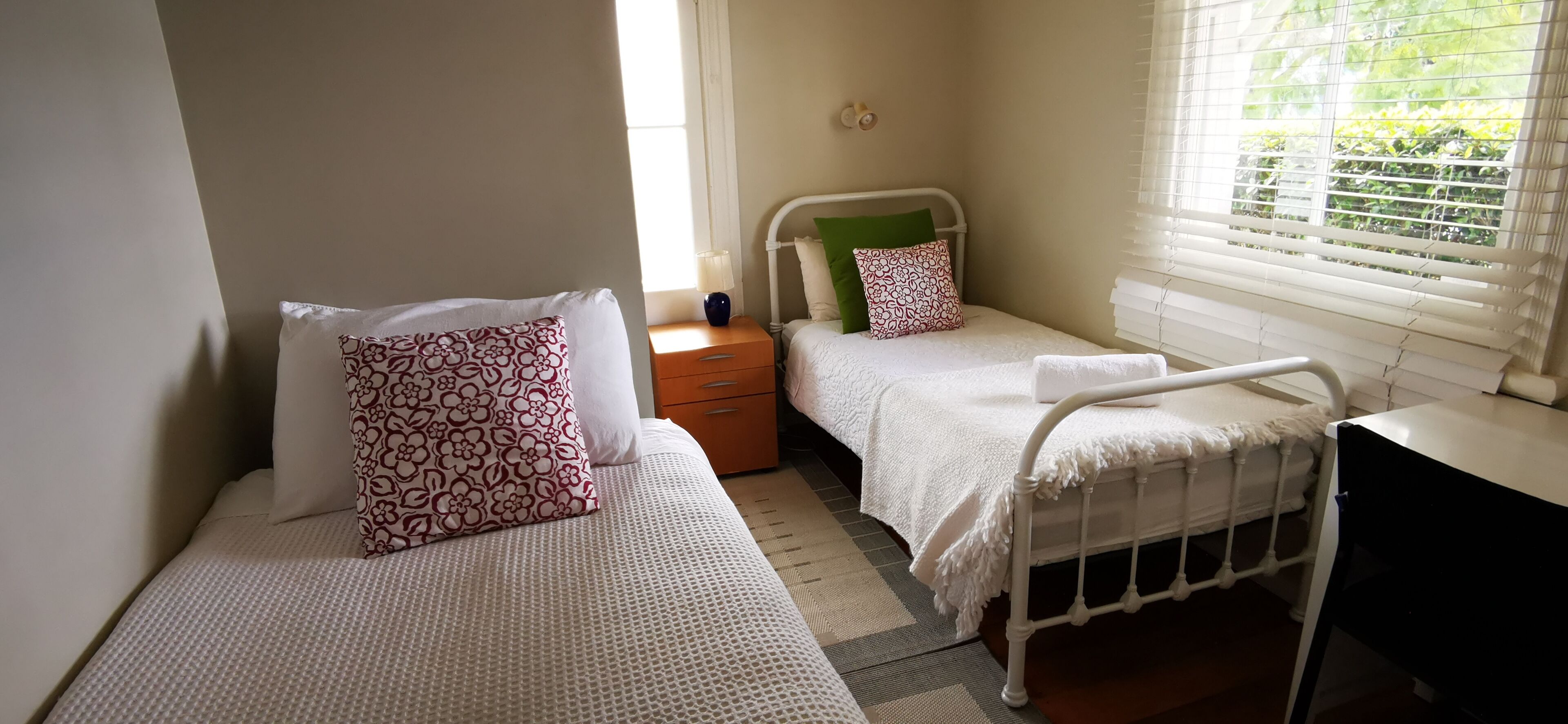 Un dormitorio con dos camas individuales, una mesita de noche y una ventana con persianas.