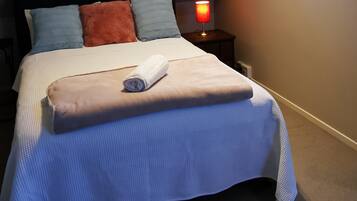 A neatly made bed with a white and blue bedspread, a rolled white towel, and a red lamp on a bedside table.
