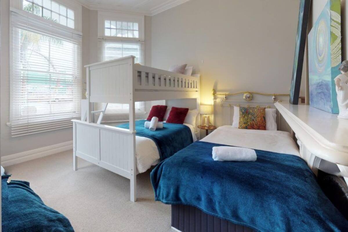A bedroom with a bunk bed, two bedside tables, a nightstand, and a window with blinds.