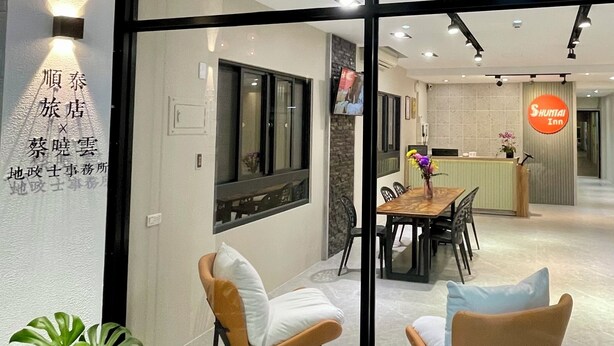 A modern hotel interior with a reception desk, a dining area with chairs and a table, and a large window with a view of the outside. - Shuntai Inn (Shoufeng)