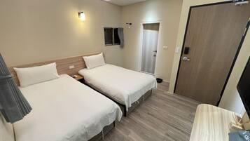 A hotel room with two beds, a desk, a chair, a TV, and a door.