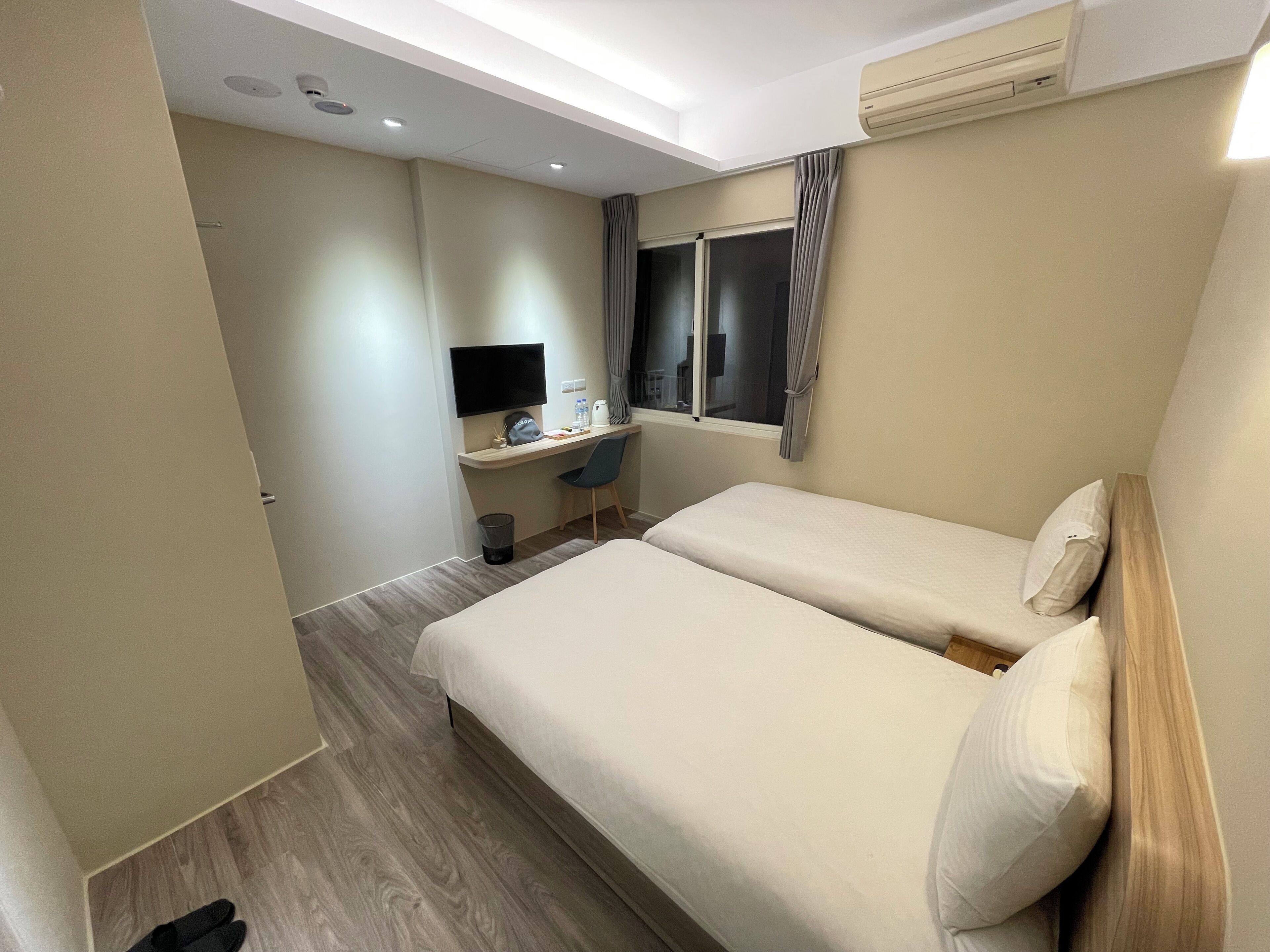 Habitación de hotel con una cama, un escritorio con computadora, una silla y una ventana con cortinas.