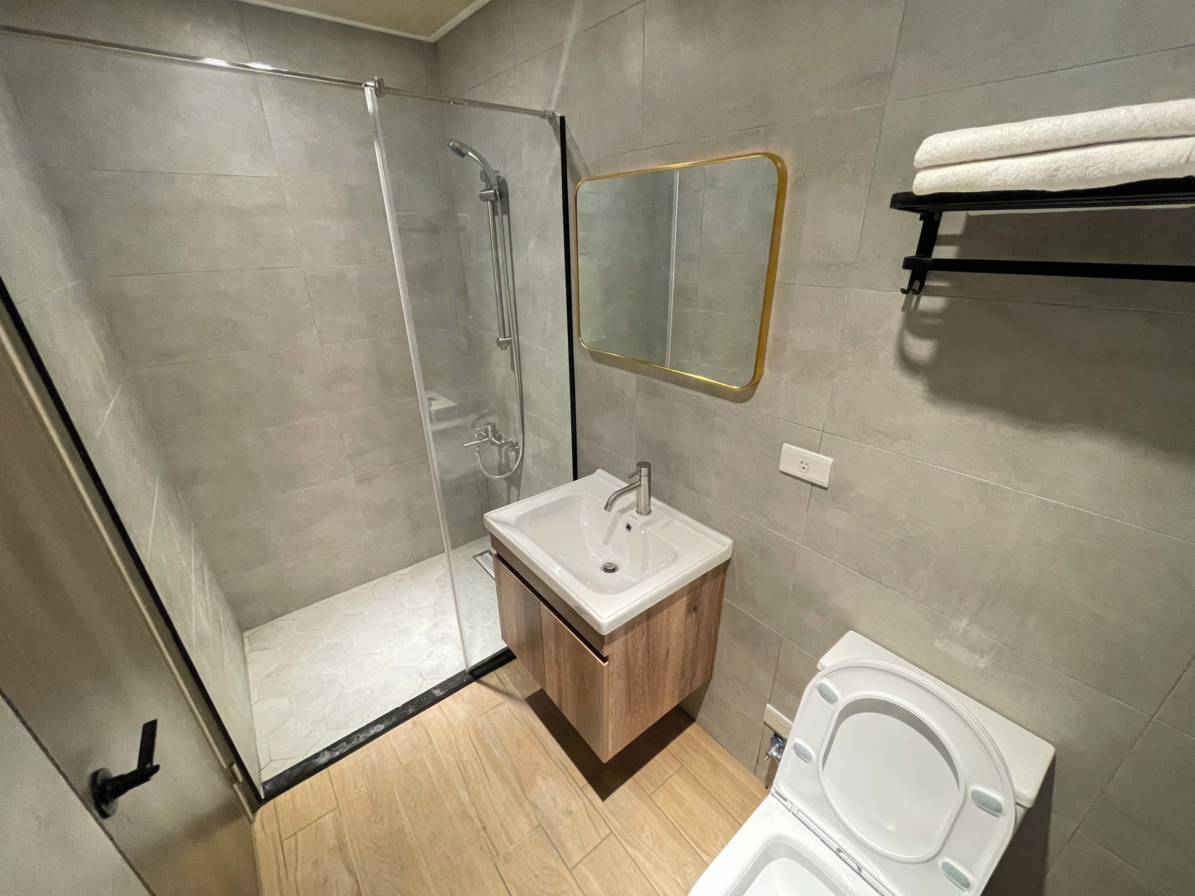 Um banheiro moderno com box de vidro, um espelho sobre bancada de madeira, pia branca, vaso sanitário e porta-toalhas.