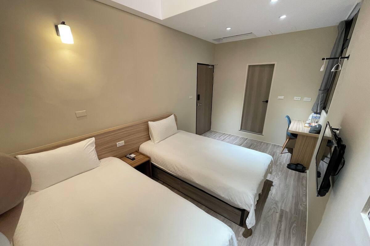 A hotel room with two beds, a desk, a chair, a TV, and a bathroom door.